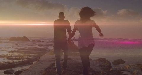 Romantic couple holding hands by the coast at sunset