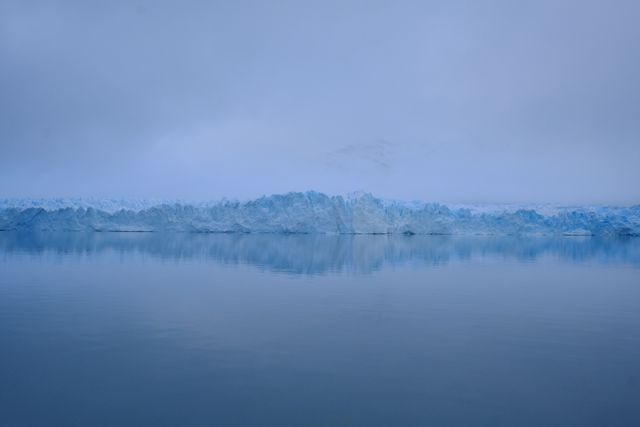 This image captures a stunning arctic landscape with blue icebergs and their reflection in calm water. Ideal for portraying themes of nature, winter, and climate change. Suitable for travel blogs, environmental articles, and advertisements focusing on adventure or exterior-related activities.