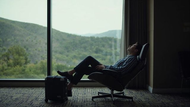 Business traveler reclining in lounge chair with suitcase by panoramic mountain window