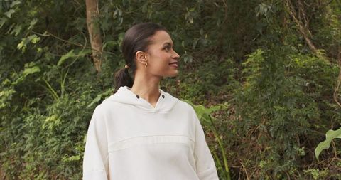 Serene woman standing on wooded hillside wearing light hoodie and hoop earrings