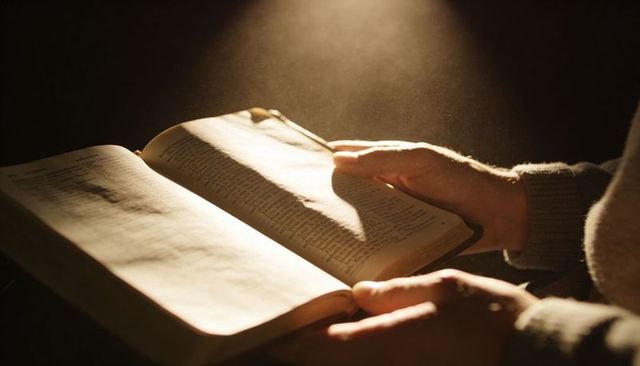 Hands holding open vintage book under warm spotlight, dust motes floating