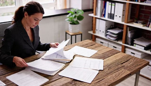 Businesswoman sorting documents at rustic desk in home office, reviewing paperwork