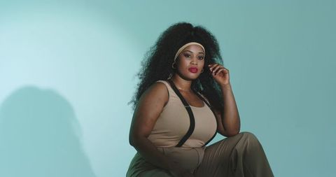 Confident african american woman posing with voluminous curls and headband against teal
