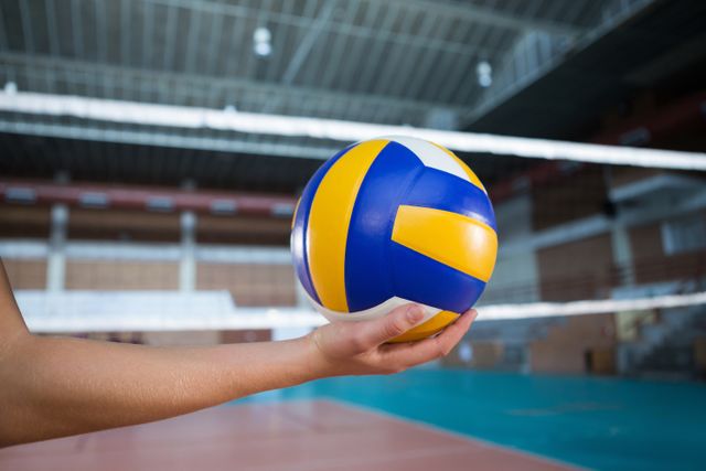 This image captures a close-up of a female player's hand holding a volleyball in an indoor court. Ideal for use in sports-related articles, fitness blogs, training manuals, and promotional materials for volleyball events or gym facilities.