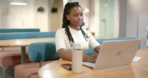 Young professional woman working on laptop in modern coworking lounge with water bottle