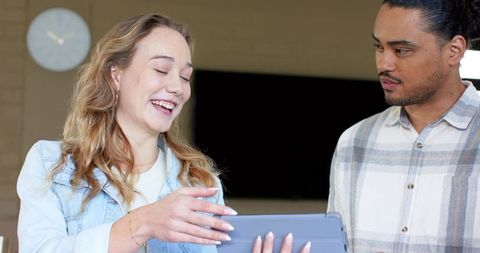 Casual coworkers sharing tablet, laughing and collaborating in modern office lounge