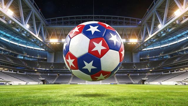 Vibrant patriotic soccer ball floating above empty stadium pitch at night under floodlights