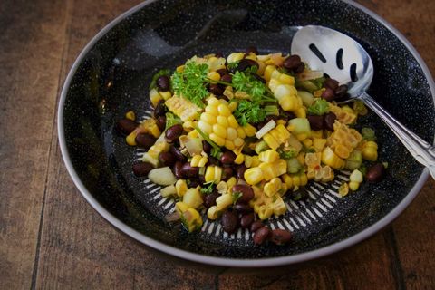 Serving vibrant corn and black bean salad with parsley on rustic black plate with spoon