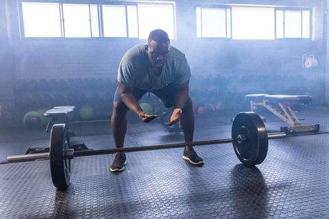 Male weightlifter preparing deadlift in moody gym with loaded barbell and chalked hands