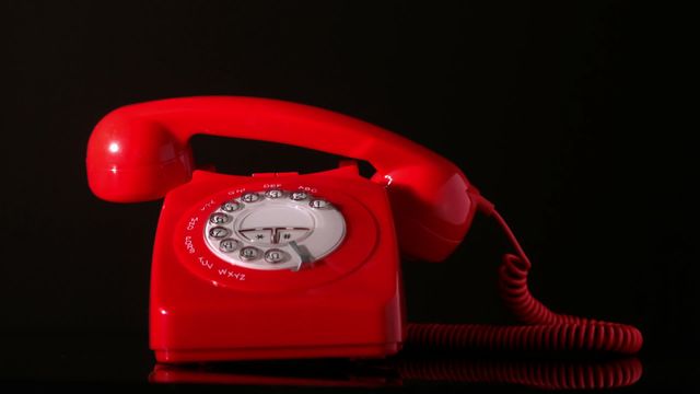 Red dial phone with receiver falling offered against a black background, showcasing vintage communication device. Useful for illustrating concepts of nostalgia, retro style, or communication technology. Perfect for themed articles, vintage-themed designs, or as a striking video in graphic projects.