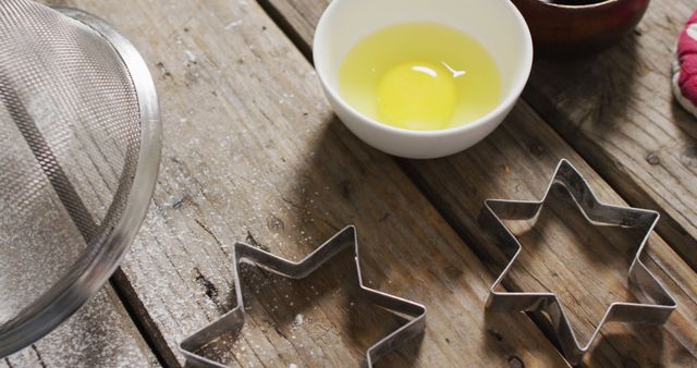Star-shaped cookie cutters, egg in bowl, and rustic wooden table. Perfect for illustrating festive baking, holiday preparation, or DIY Christmas cookie recipes.