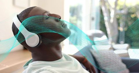 Reclining man wearing headphones listening to music with teal soundwave in living room