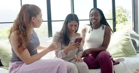 Friends comforting tearful woman holding smartphone on couch in sunlit living room
