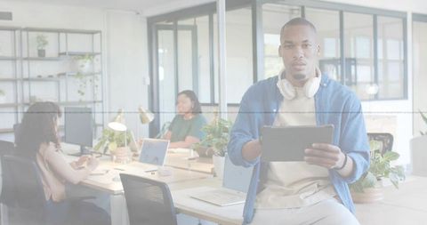 Young professional holding tablet wearing headphones sitting on desk in modern sunlit coworking spac