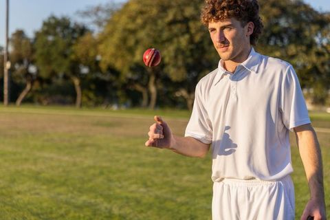 Young cricketer bowling red leather ball on sunny field practicing focused delivery