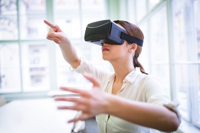 Female graphic designer gesturing while using virtual reality headset in office