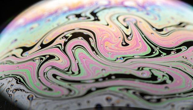 Iridescent soap film macro showing colorful swirling marbling, black bands, droplets
