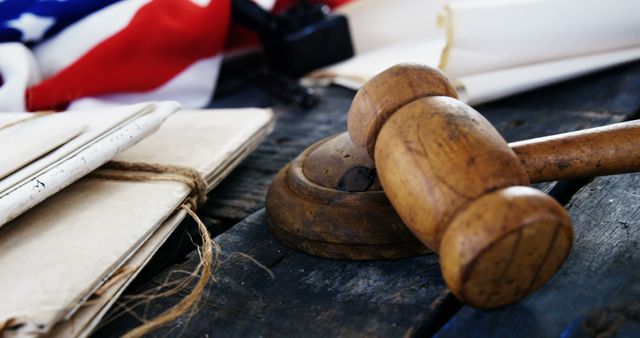 A wooden gavel rests on its sound block beside a folded American flag and old documents, symbolizing the American justice system and historical legal foundations. The arrangement evokes a sense of tradition and patriotism within the context of law and governance.