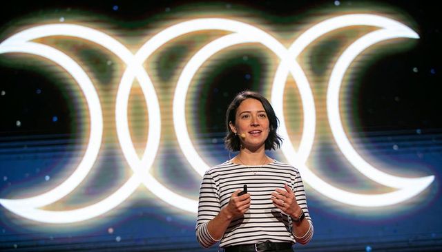 Woman presenting keynote at tech conference with illuminated crescent rings led backdrop