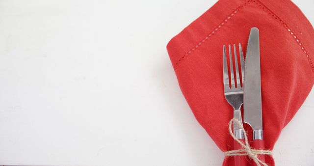 A fork and knife are neatly wrapped in a red napkin, with copy space. This setup suggests a dining scene, in preparation for a meal or a festive occasion.