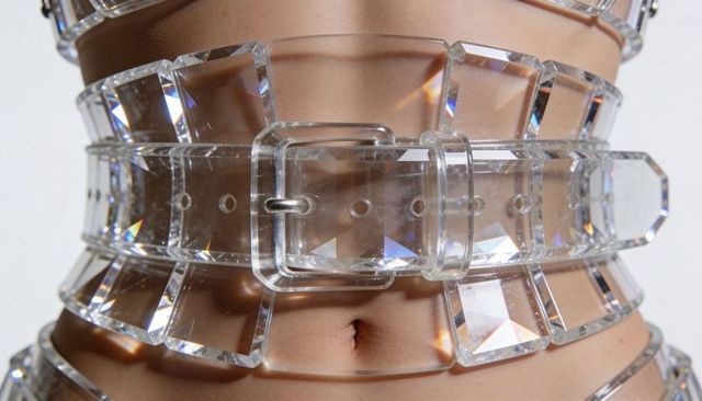 Female torso wearing clear faceted acrylic belts creating crystal prism refractions at waist