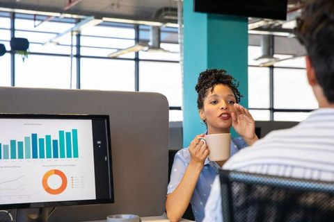 African american woman holding mug discussing data with coworker in open-plan office