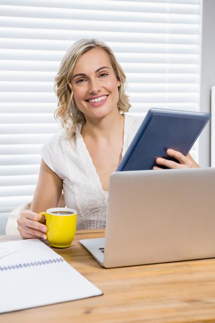 Portrait of beautiful woman holding digital tablet and coffee mug at home