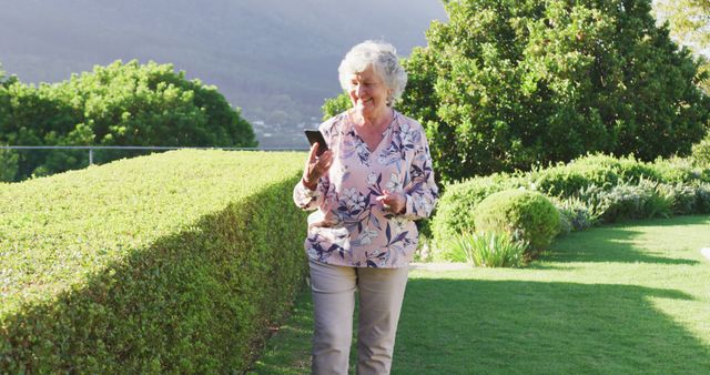 Caucasian senior woman smiling while talking on smartphone while walking in the garden. retirement senior lifestyle living concept