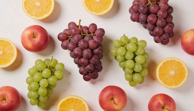 Vibrant mixed fruit flatlay featuring red and green grape bunches, orange halves, apples