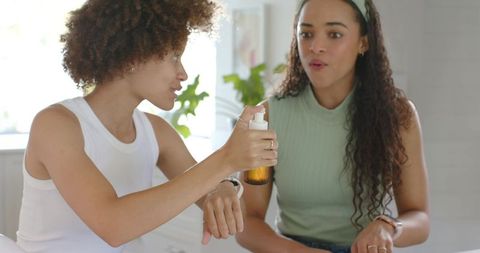 Friends sharing skincare serum and testing moisturizer on wrist for natural glow self care