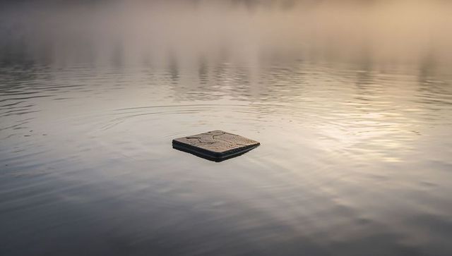 Floating square slab creating gentle concentric ripples on mist-covered lake at golden dawn