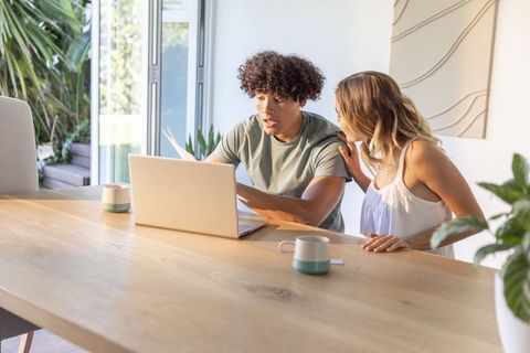 Young diverse couple reviewing bills and finances on laptop at sunlit modern dining table
