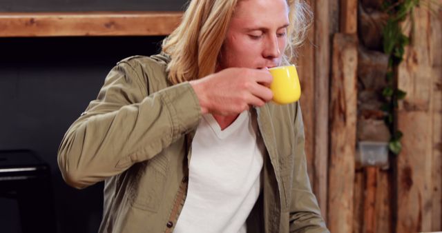 Caucasian man with long blonde hair sitting at table in cafe drinking coffee. Free time, refreshment, convenience and cafe, unaltered.