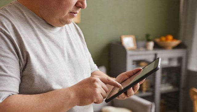 Middle-aged man tapping tablet screen at home in cozy modern interior