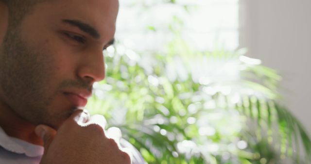 Man contemplating or deep in thought, with natural sunlight and lush green plants in background. Suitable for content around mindfulness, decision-making, stress relief, mental health, focus, or mental clarity.