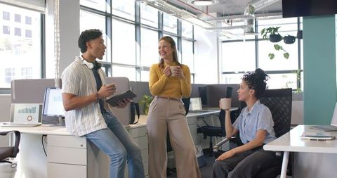 Diverse team chatting in sunlit modern open-plan office during coffee break