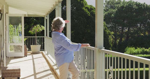 An elderly woman standing on a porch, smiling while enjoying the sunlight over a lush garden. The image conveys themes of relaxation, retirement, and the joy of spending time outdoors. Suitable for use in marketing materials for senior living communities, retirement planning, and health and wellness programs.