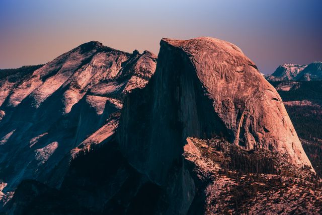 This image showcases the famous Half Dome rock formation in Yosemite National Park during sunset. The warm lighting emphasizes the dramatic contours of the rock and provides a contrast against the shadowed crevices. This stunning view highlights the beauty of California's wilderness, making it ideal for travel guides, nature blogs, and promotional materials for outdoor adventure companies.