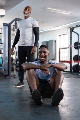 Trainer coaching smiling client resting after heavy strength set in modern gym