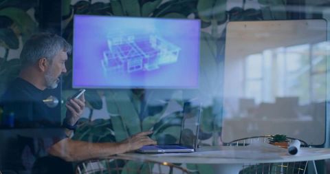 Architect holding phone and working on laptop in glass meeting room with blueprint display
