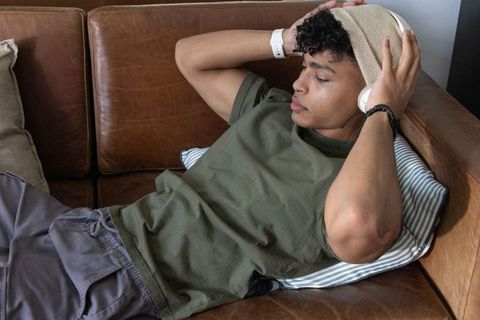 African american man reclining on leather sofa wearing beanie and adjusting headphones