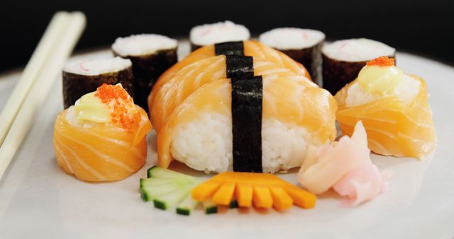 A plate of assorted sushi and sashimi, including nigiri topped with salmon and rolls with various fillings, is presented with chopsticks to the side, with copy space. Sushi, a traditional Japanese dish, has gained worldwide popularity for its fresh flavors and artistic presentation.
