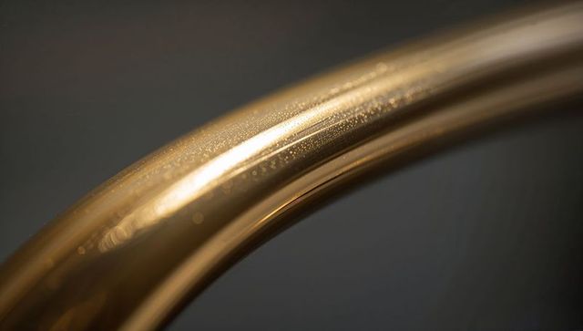Glinting curved brass rail reflecting droplets and specular highlights for luxury branding