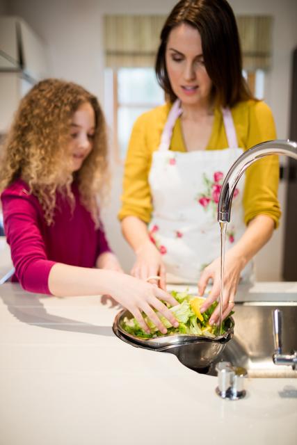 Mother assisting daughter in washing lettuce in kitchen - Download Free Stock Photos Pikwizard.com