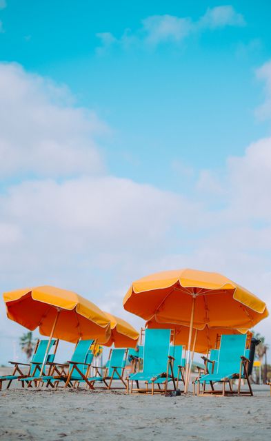 This vibrant scene showcasing orange umbrellas and blue chairs on a sandy beach invokes a sense of relaxation and vacation. Great for promoting tourism, travel brochures, vacation websites, and advertisements related to summer holidays, beachfront resorts, and coastal retreats.