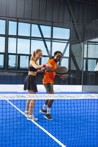 Coach guiding student on padel court with rackets indoors