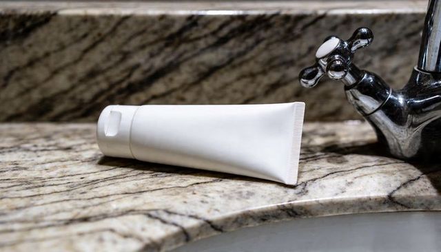 Blank white squeeze tube on marble vanity with chrome faucet for cosmetic branding mockup