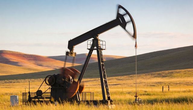 Pumping oil pumpjack swinging walking beam over grassy prairie at golden hour sunrise