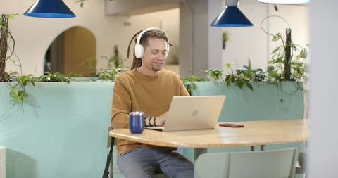 African american freelancer working in biophilic coworking space wearing headphones using laptop
