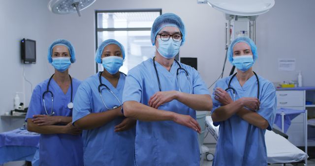 Four healthcare professionals stand in an operating room, wearing blue scrubs, caps, masks, and stethoscopes, demonstrating confidence and readiness. This image can be used for healthcare promotions, hospital advertisements, medical training materials, and recruitment campaigns. Illustrates commitment, professionalism, and teamwork in a clinical setting.